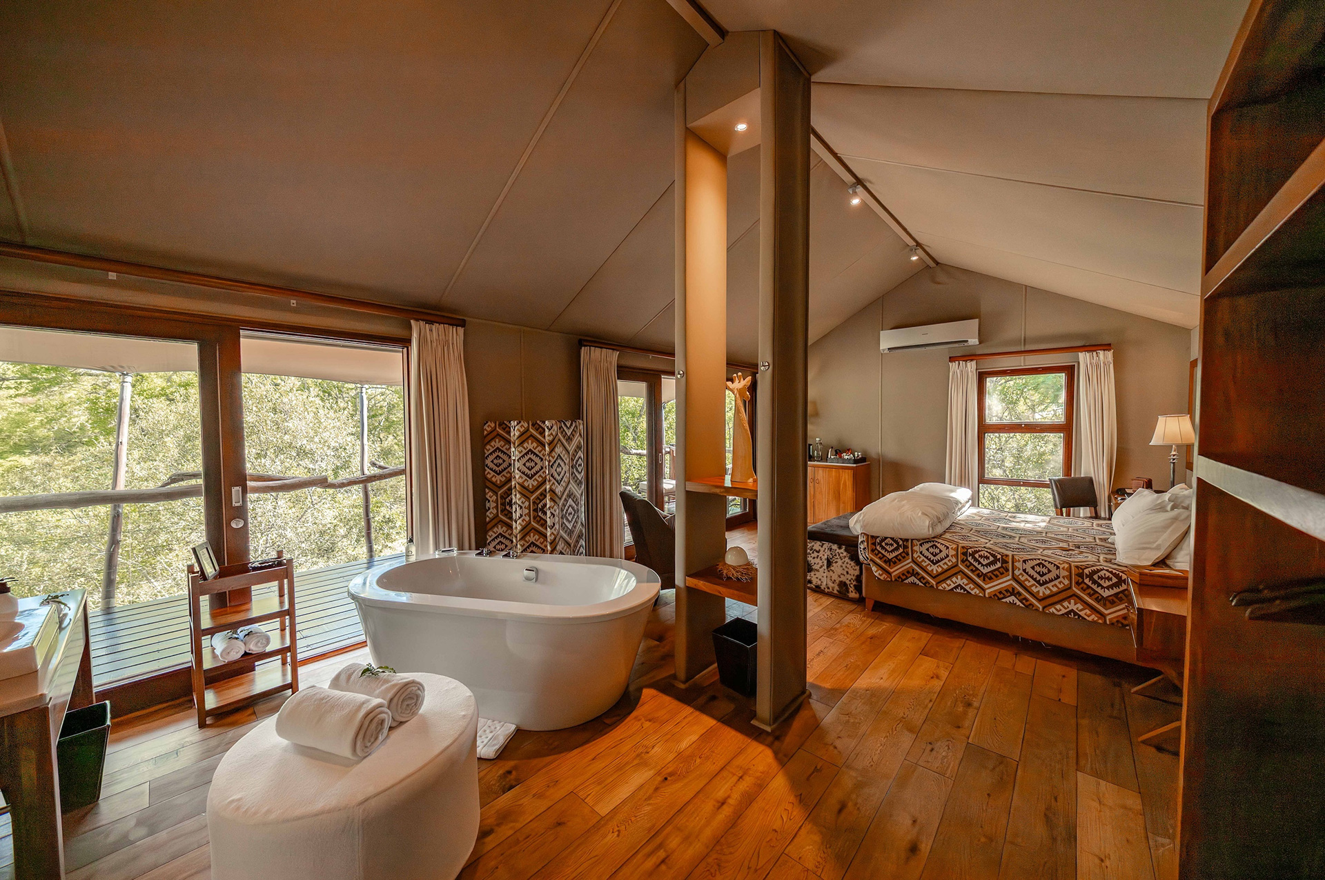 Tented safari suite with wooden floors, freestanding bathtub, patterned bedding, and forest-view balcony at Kapama Buffalo Camp.