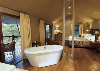 Elegant safari tent suite featuring a freestanding bathtub, cozy lounge area, king-size bed with tribal-print bedding, and private deck overlooking the bushveld.