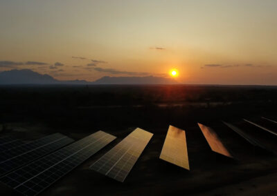 Aerial view of solar panel array at sunset, located alongside a remote highway with mountains in the background.